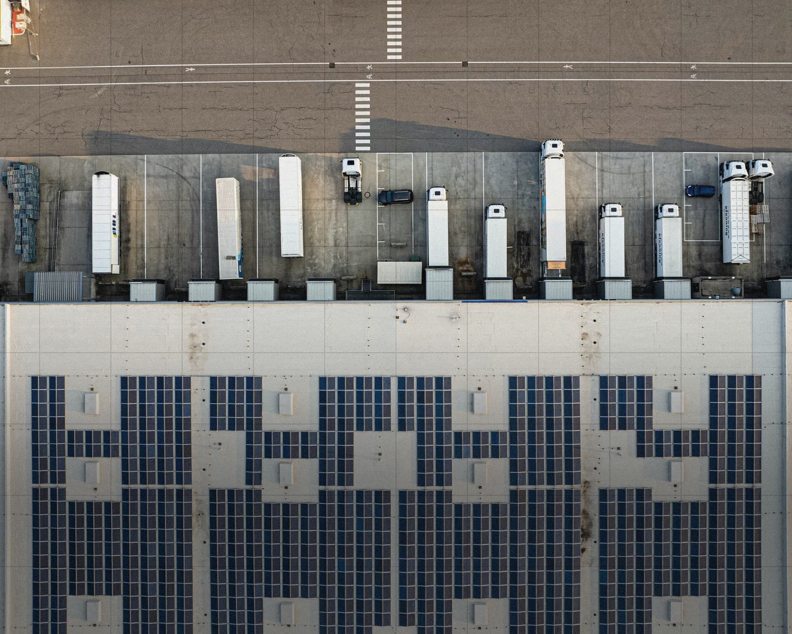 Aerial view of a logistics warehouse with a solar roof and trucks at the loading docks.