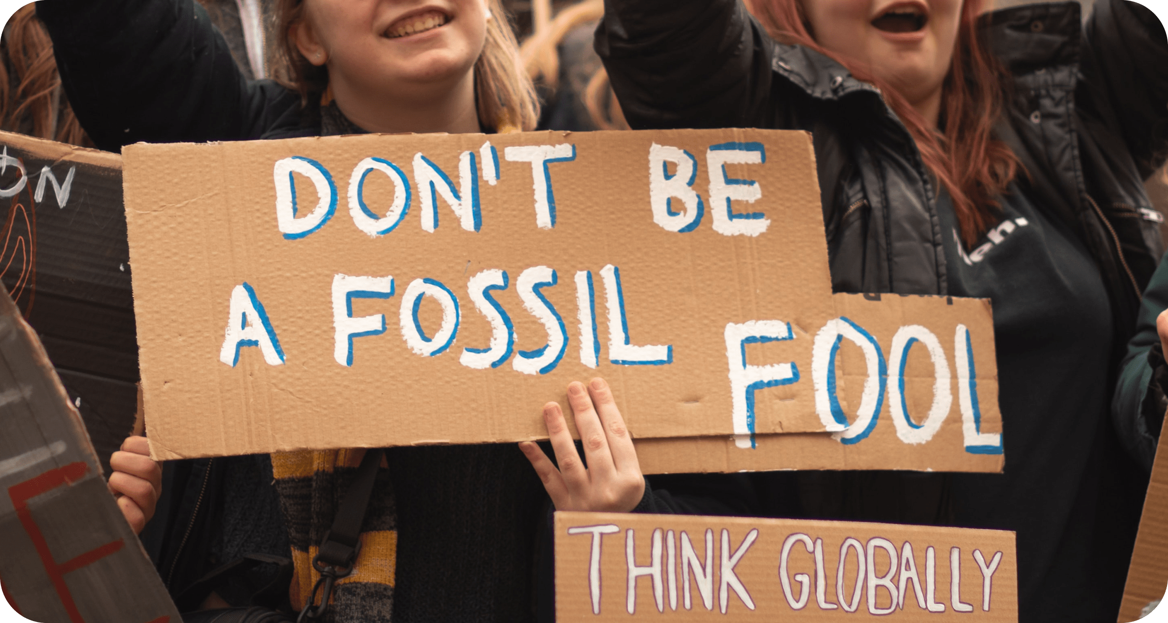 Climate protestor holding a cardboard sign reading 'don't be a fossil fool'